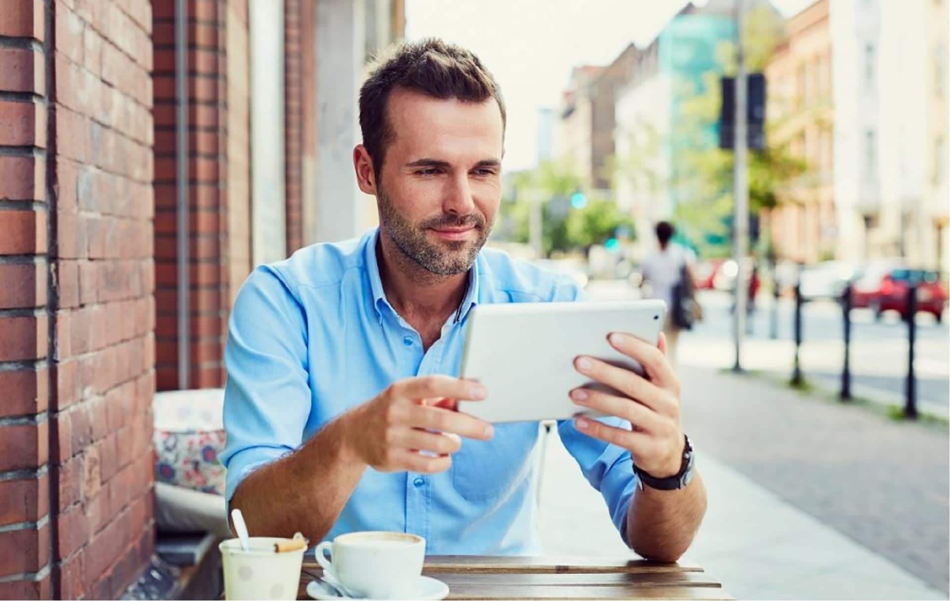 Homme assis à la terrasse d'un café avec tablette en main